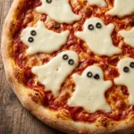 Five vegan pizzas topped with melted white vegan cheese shaped like ghosts with olive eyes and mouths on red sauce.
